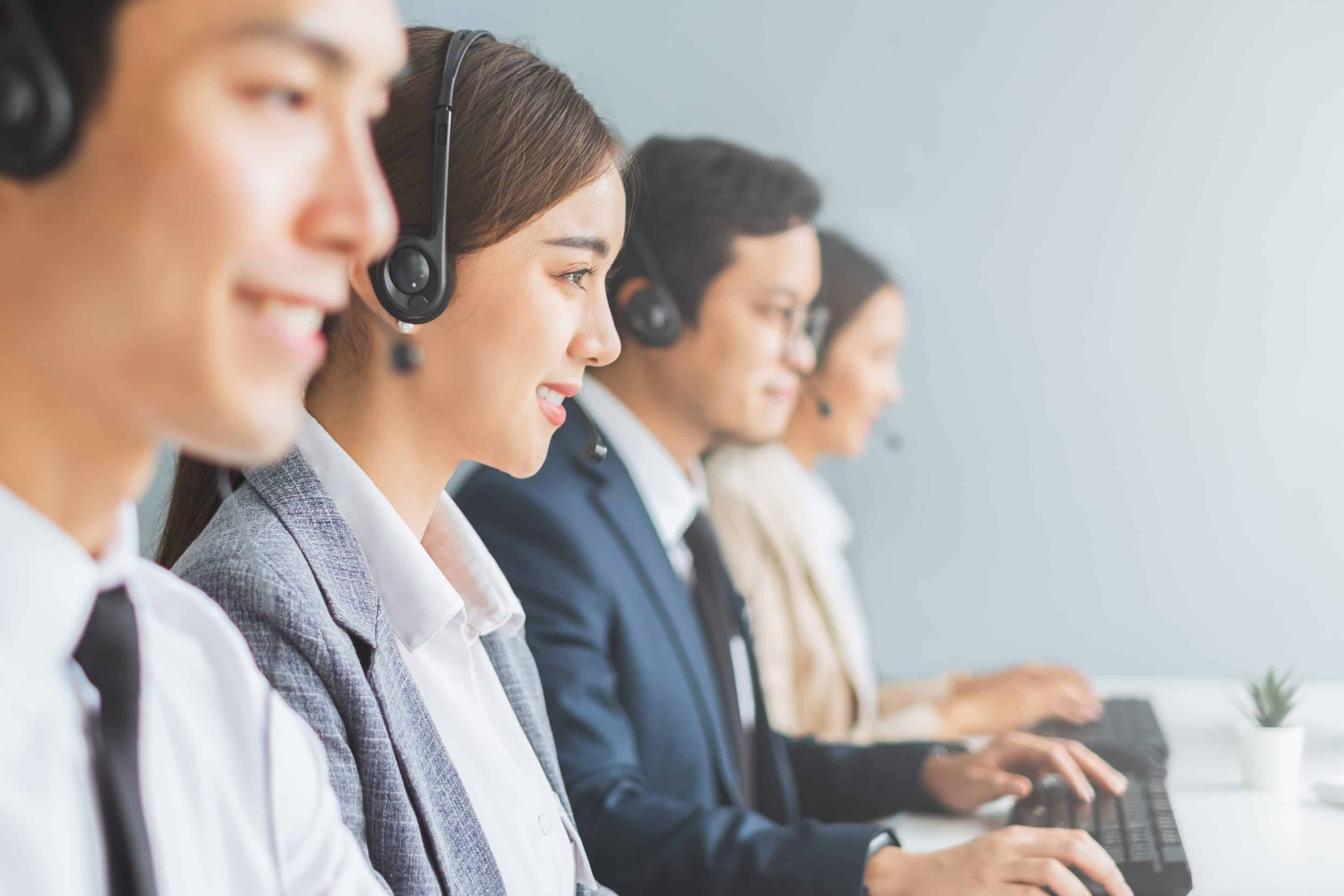 Asian call center team customer service telesales in formal suit wearing headset or headphone talking with customer in modern office
